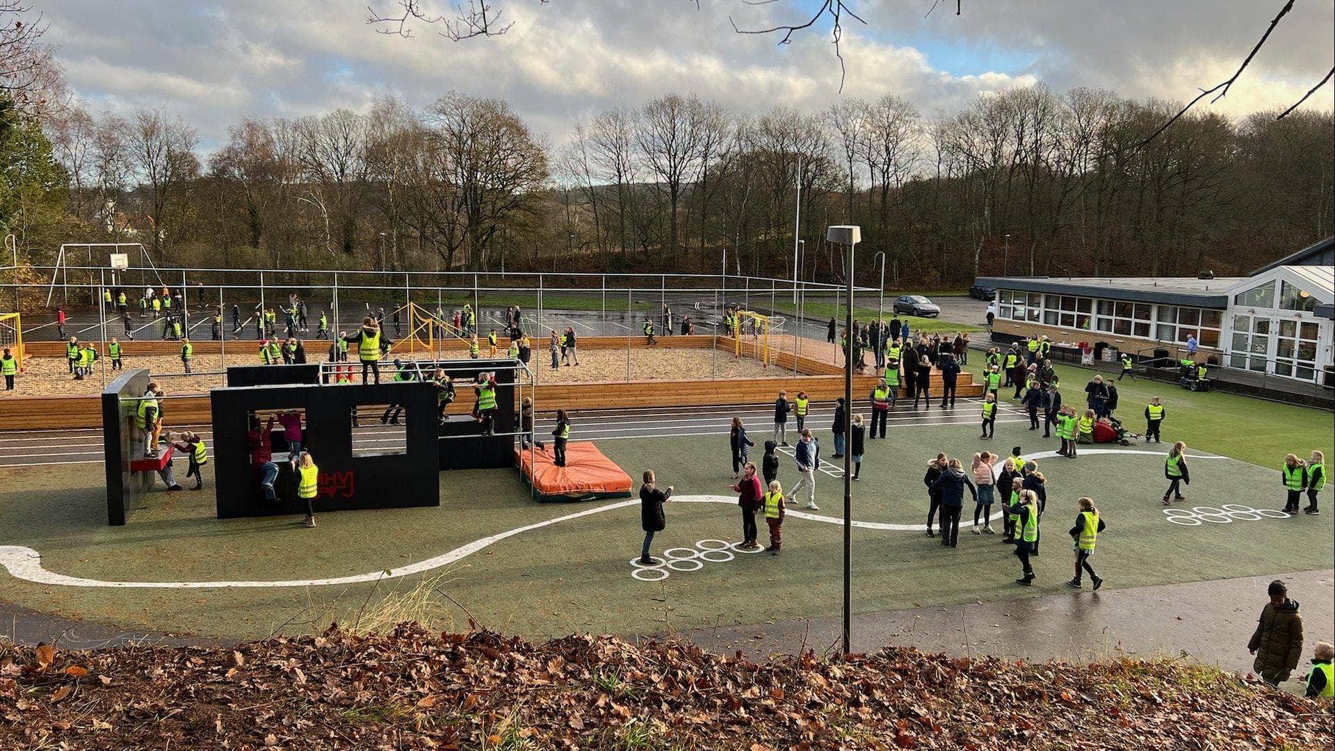 Parkouranlæg med sorte moduler, rød platform og børn samt voksne på kunstgræsunderlag